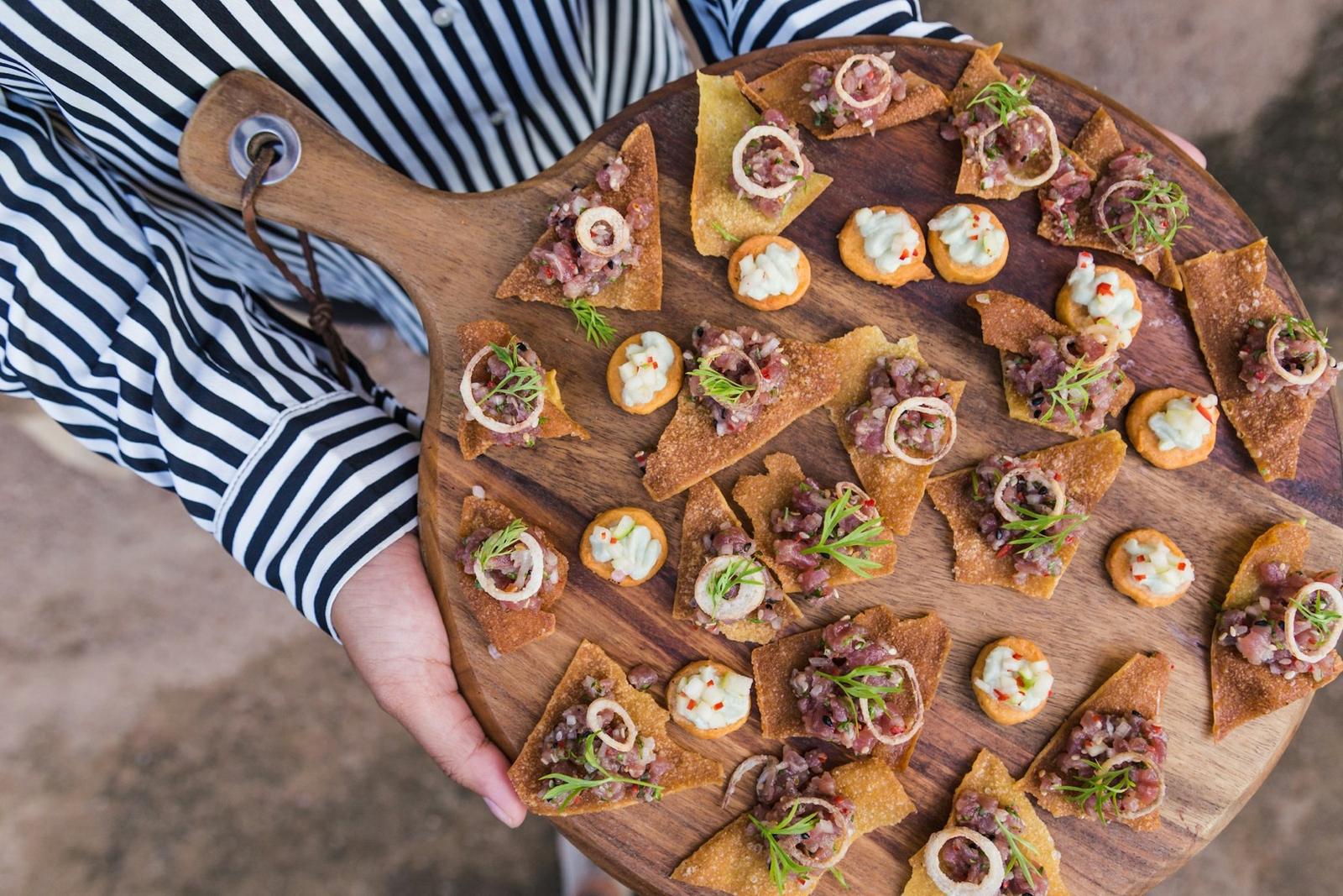 A server holding a wooden board of canapés
