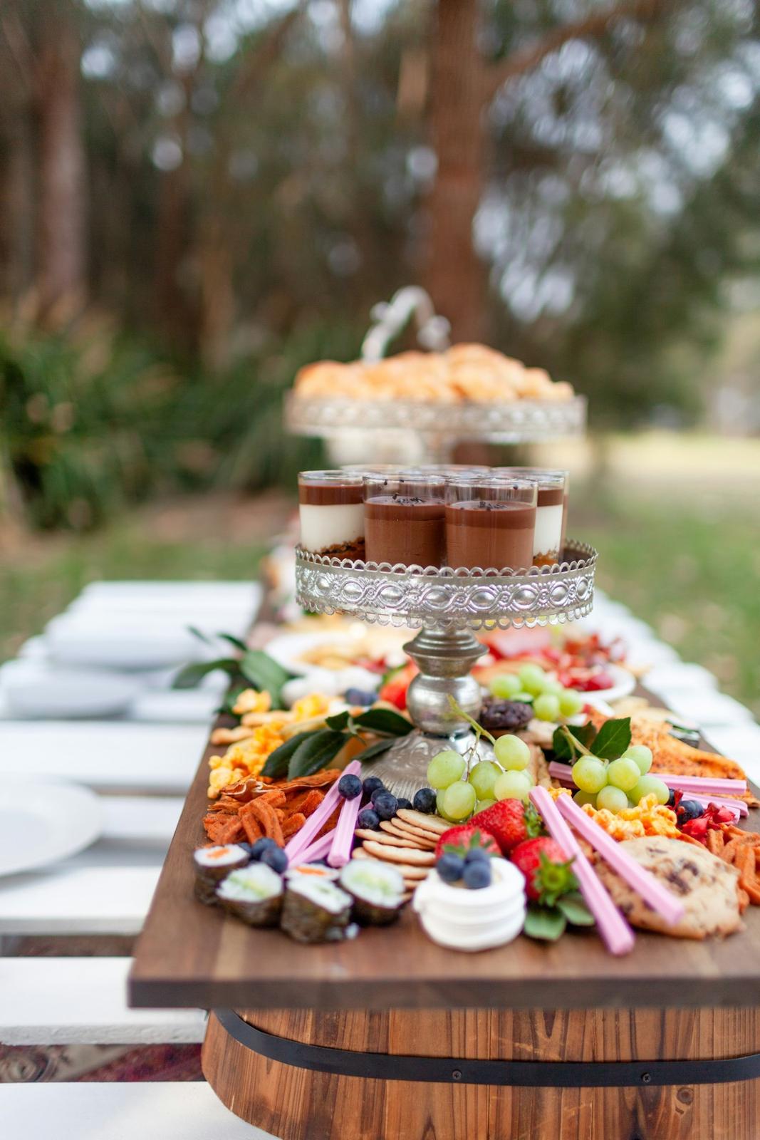 A grazing table of cheese, fruit and bread laid on a wooden table in a garden