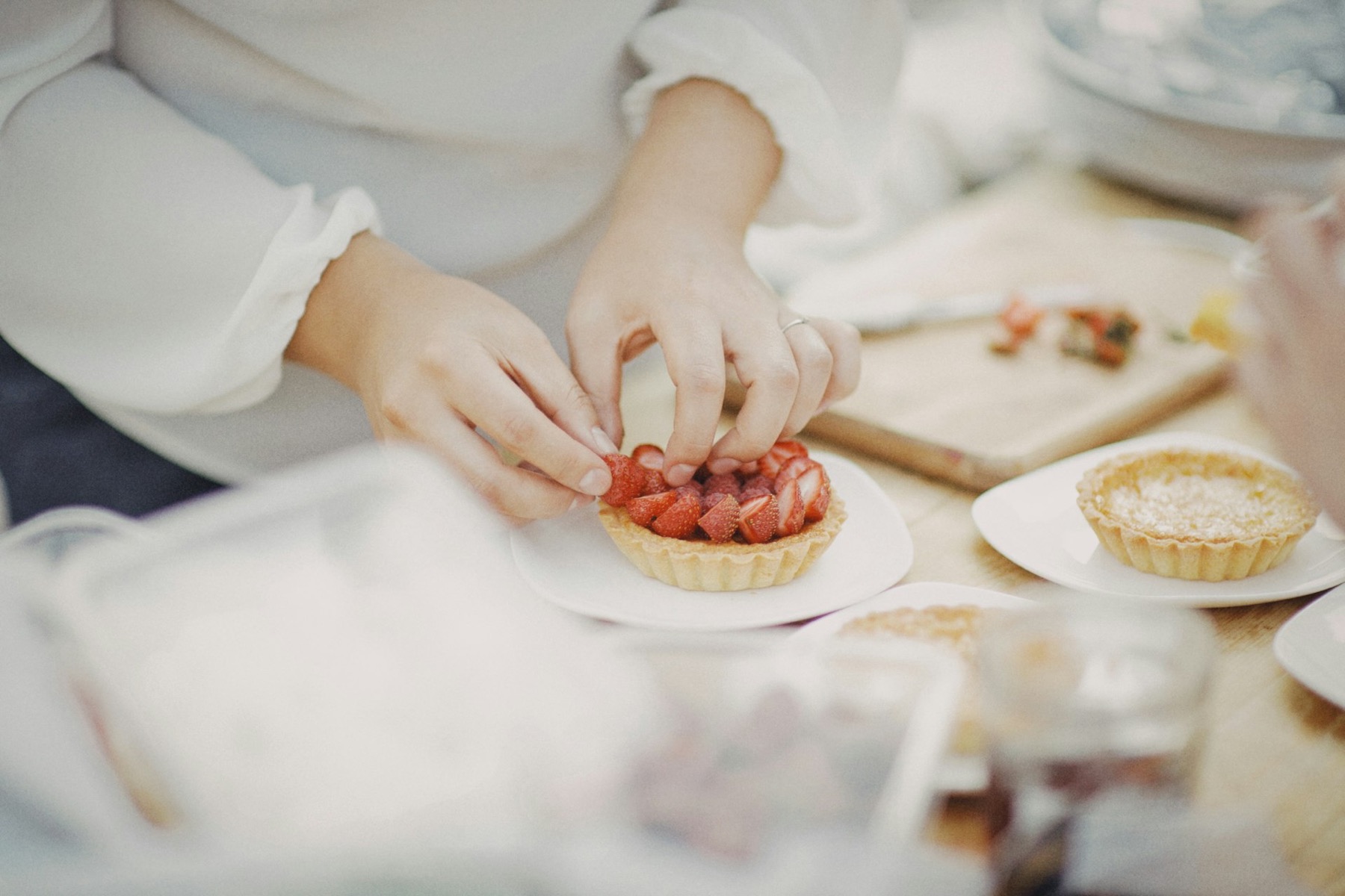 Hands filling small tart cases with fruit