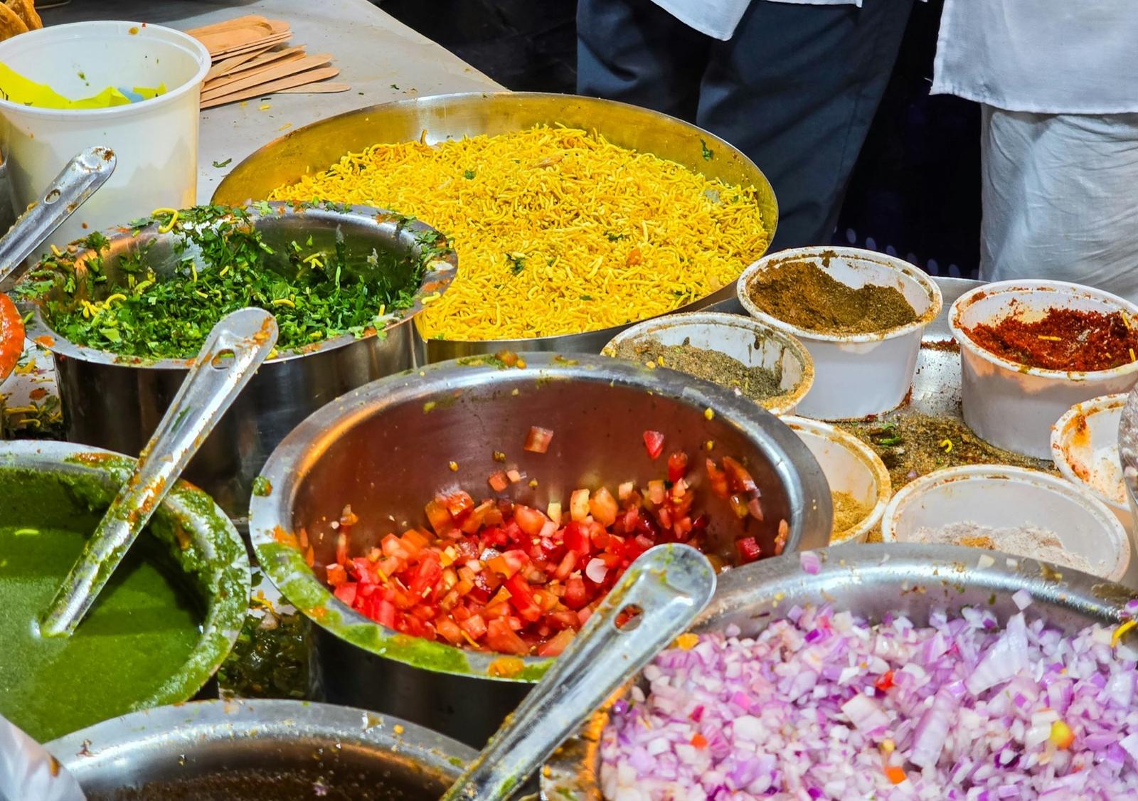 Bowls of chutneys, sev and chopped onion at a chaat counter