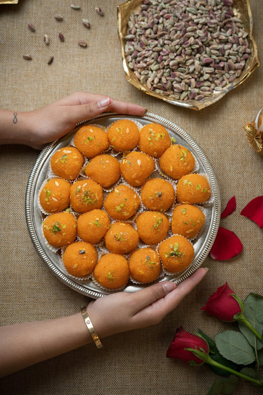 Hands holding a brass plate of motichoor laddoo