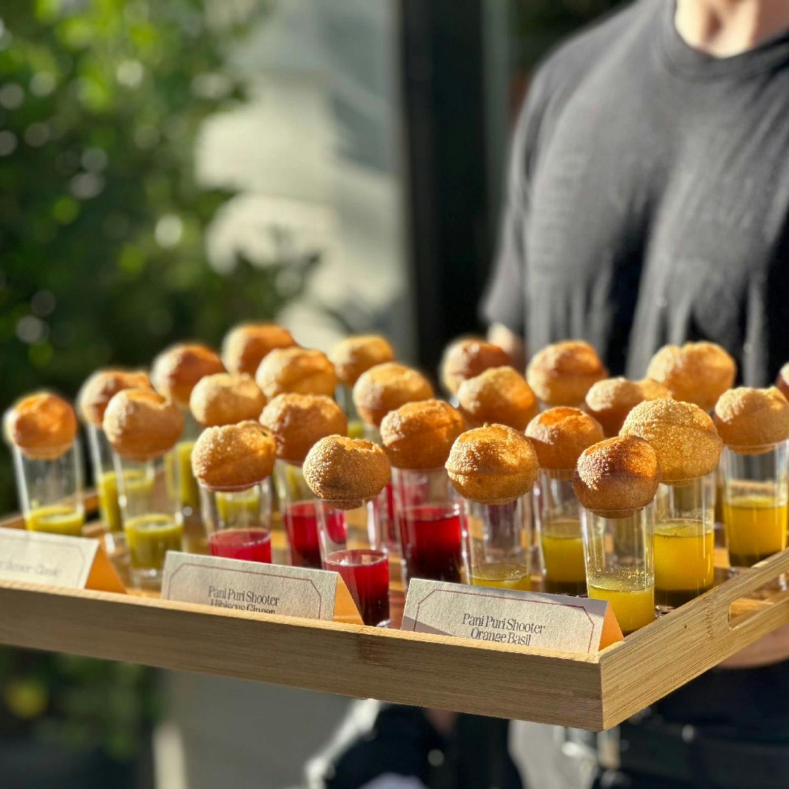 Pani puri served in shot glasses on a wooden tray