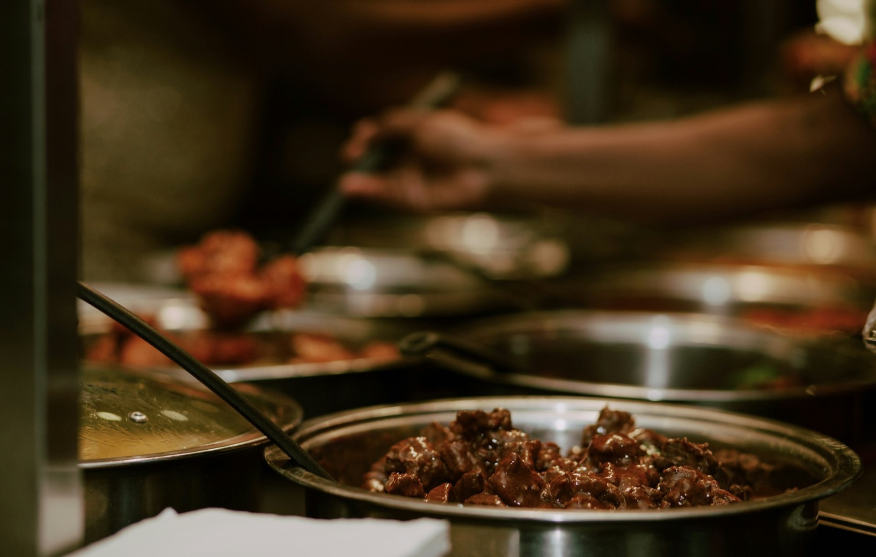 A server ladling food from a steel buffet tray